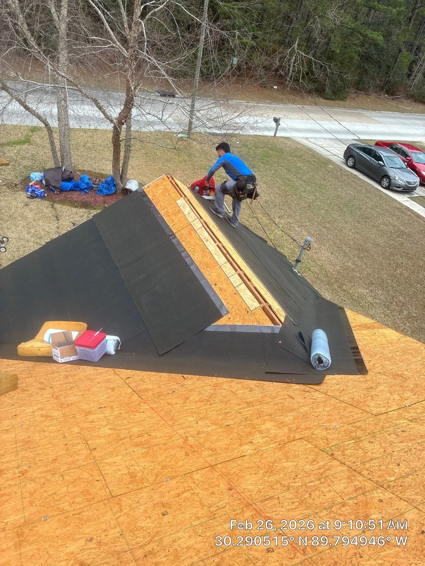 Roofing crew member installing underlayment on exposed roof decking